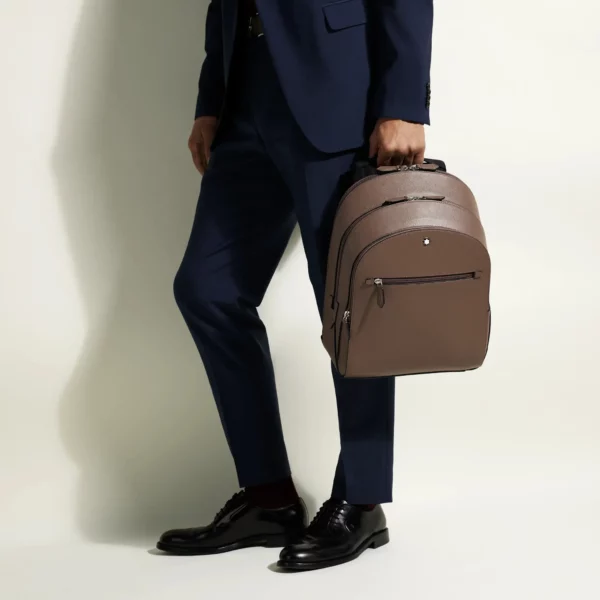 Uomo elegante porta a mano uno zaino Montblanc in pelle Saffiano colore mastice.