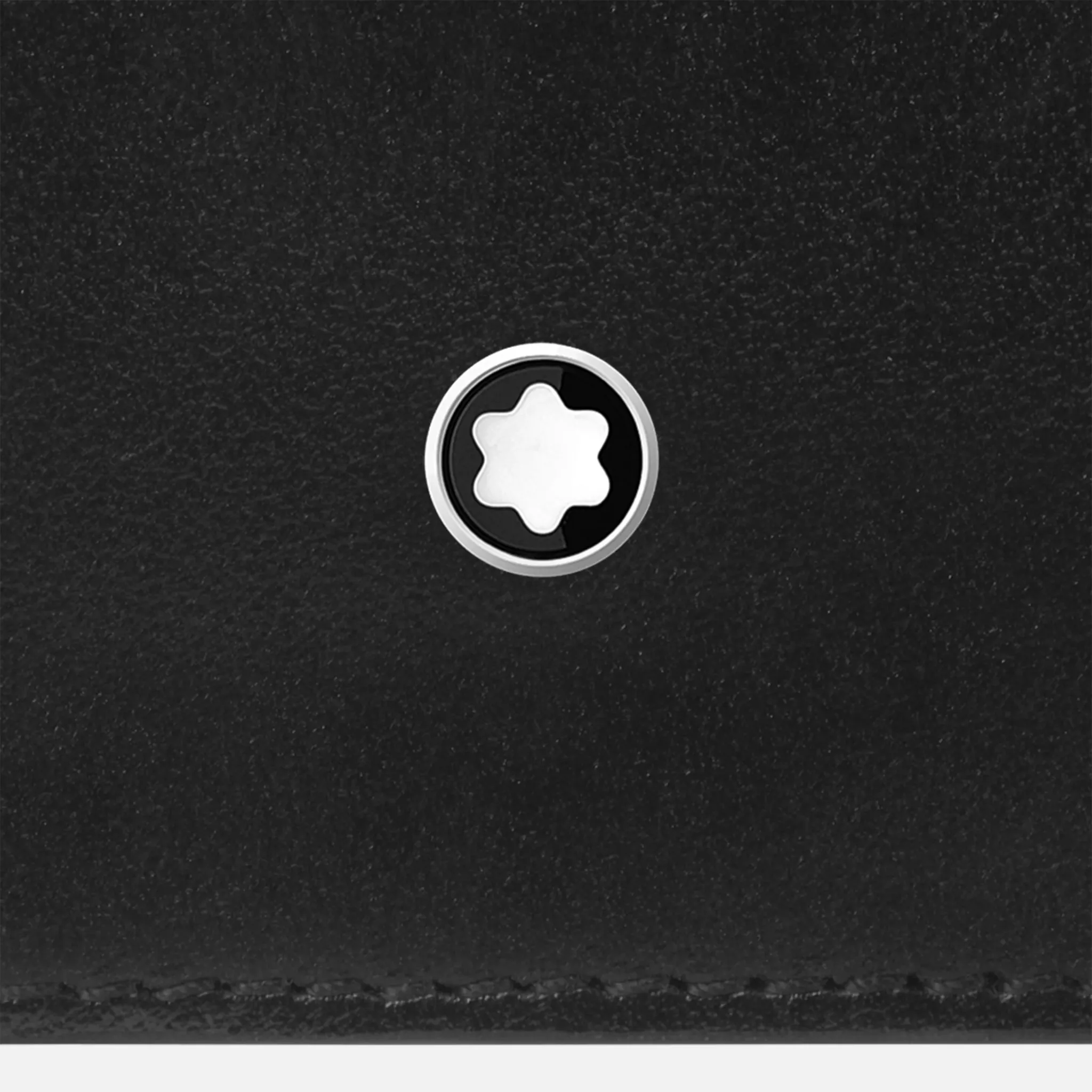 Primo piano dell’emblema Montblanc a stella bianca incastonato sul portafoglio in pelle nera.