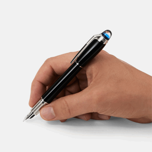 Mano che impugna una stilografica Montblanc StarWalker nera con dettagli in metallo e cappuccio azzurrato, pronta a scrivere su superficie bianca.