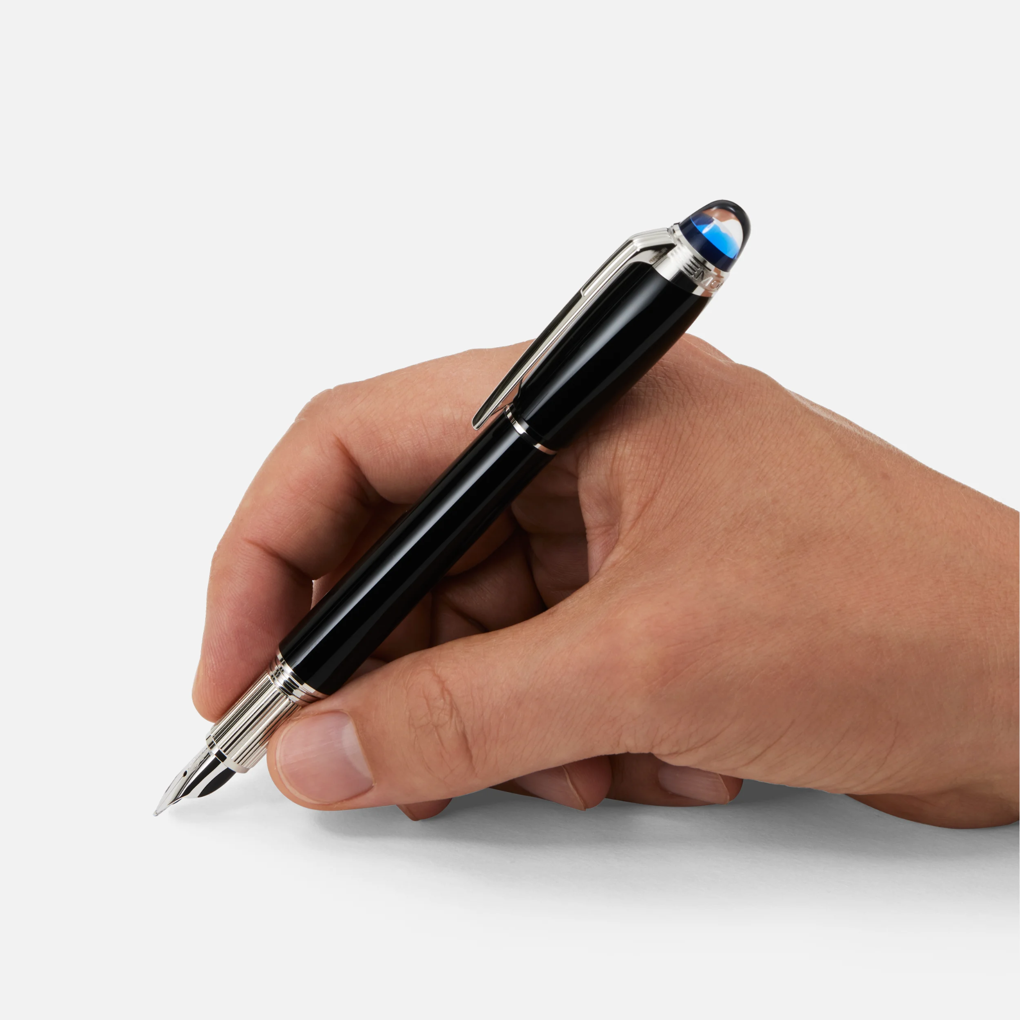Mano che impugna una stilografica Montblanc StarWalker nera con dettagli in metallo e cappuccio azzurrato, pronta a scrivere su superficie bianca.