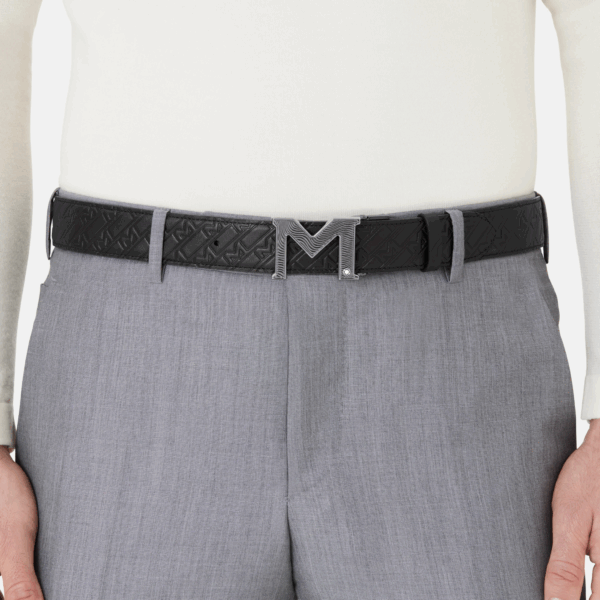 Cintura Montblanc reversibile in pelle nera con fibbia M guilloché indossata su pantaloni grigi