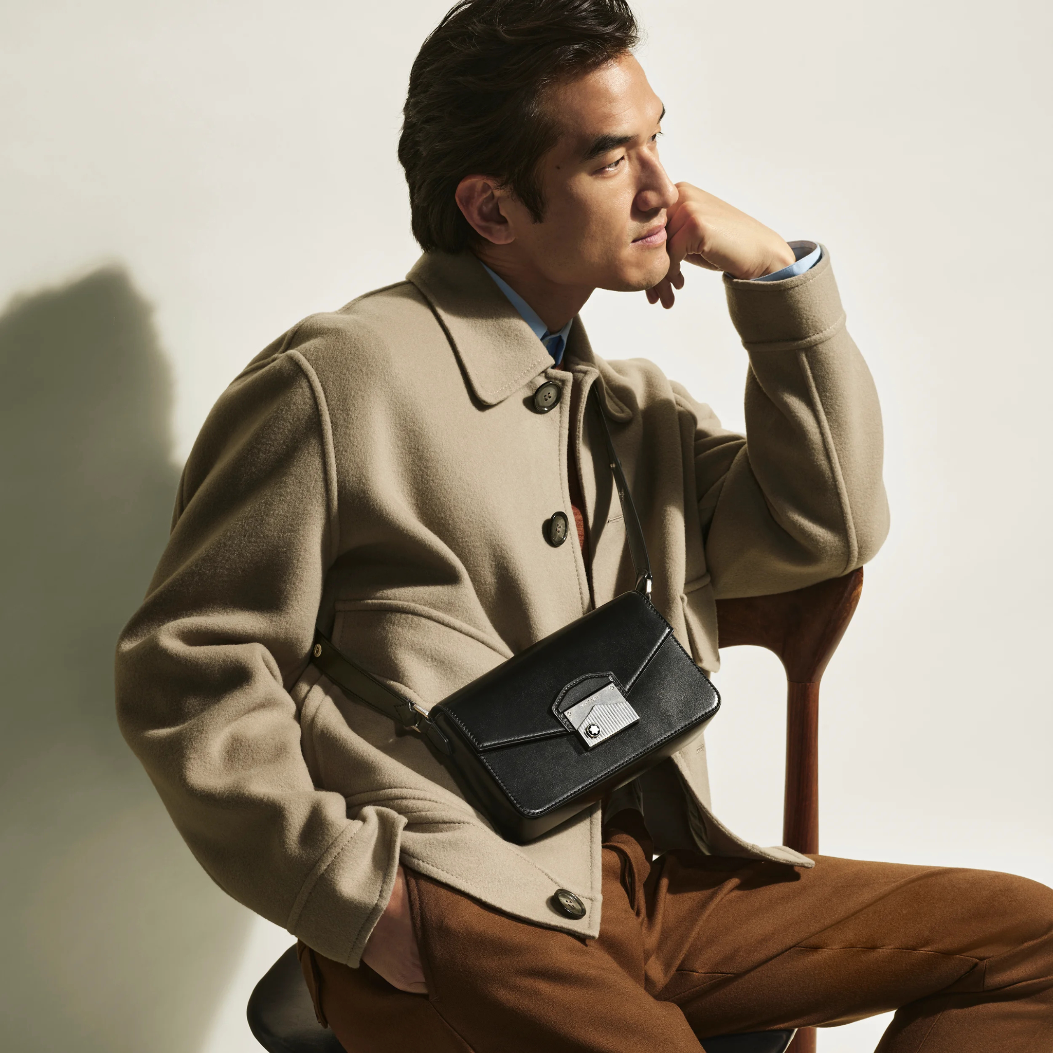 Persona seduta con cappotto beige e borsa crossbody Montblanc nera con chiusura argentata